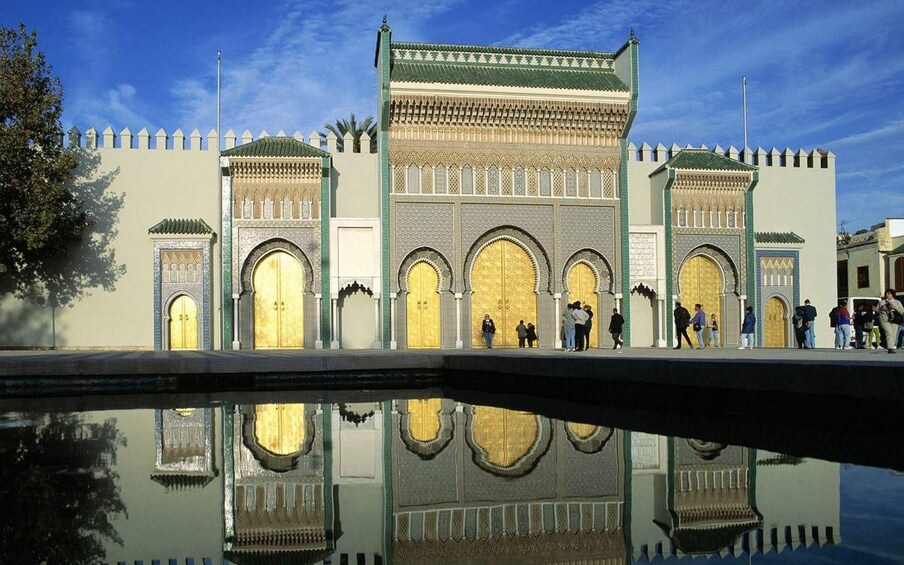 A historic building with arched doorways and intricate tile work, reflecting in a pool. 1