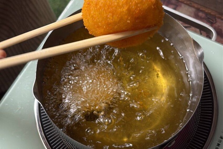 A hand holding a fried item over a pan of hot oil. 4