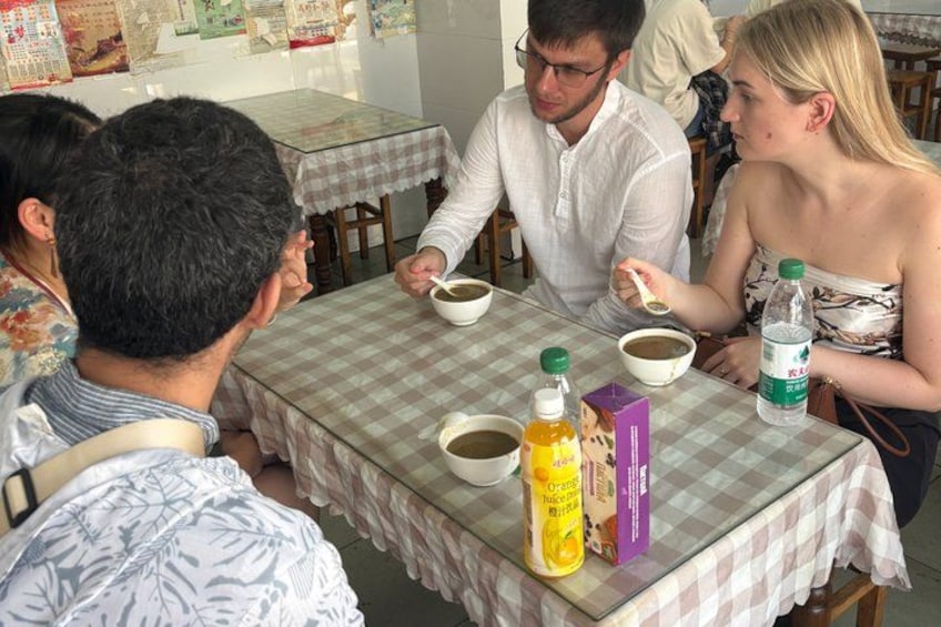 A group of people dining at a restaurant with checkered tablecloths, bowls of food, and bottles of beverages. 3