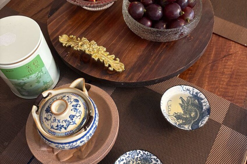 A wooden table with a teapot, a bowl of grapes, and a decorative plate. 2