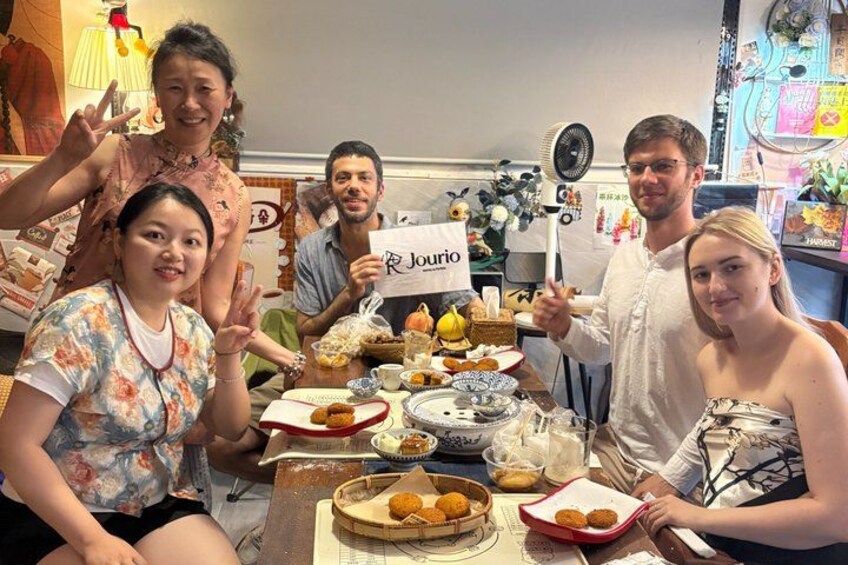 A group of people sitting around a table with various dishes and a sign that reads 'Jourio'. 2