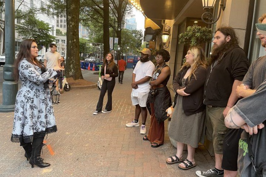 A group of people standing on a sidewalk, some engaged in conversation. 4