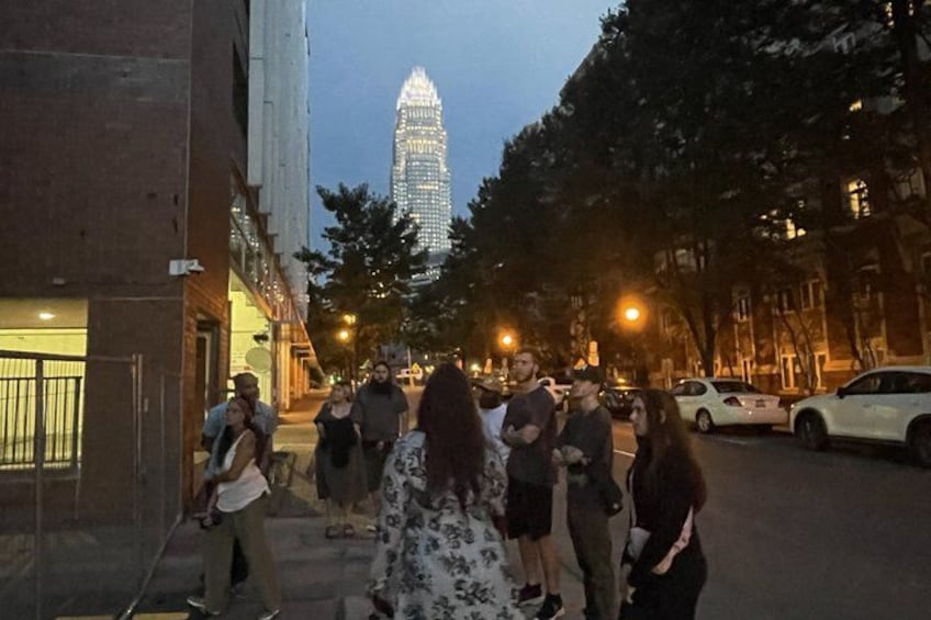 A group of people walking on a city street at dusk, with a tall building in the background. 3