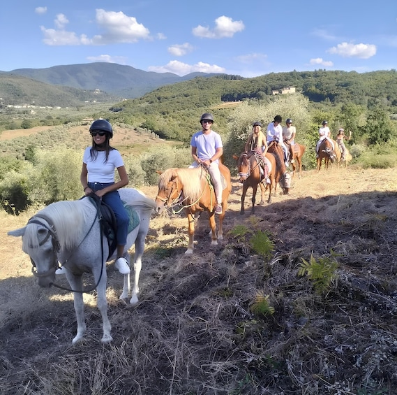 A group of people horseback riding on a dirt trail with a mountainous backdrop. 1