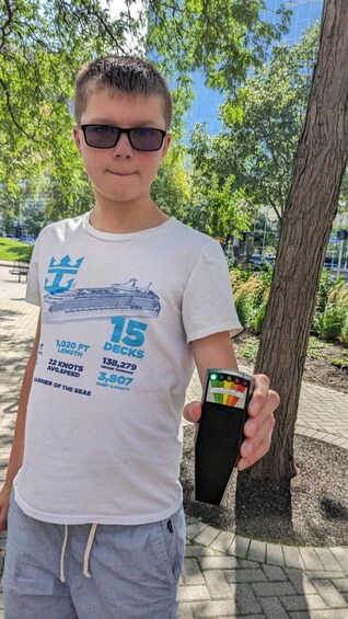 A person holding a device with a gauge, standing in a park with trees and a paved path. 2