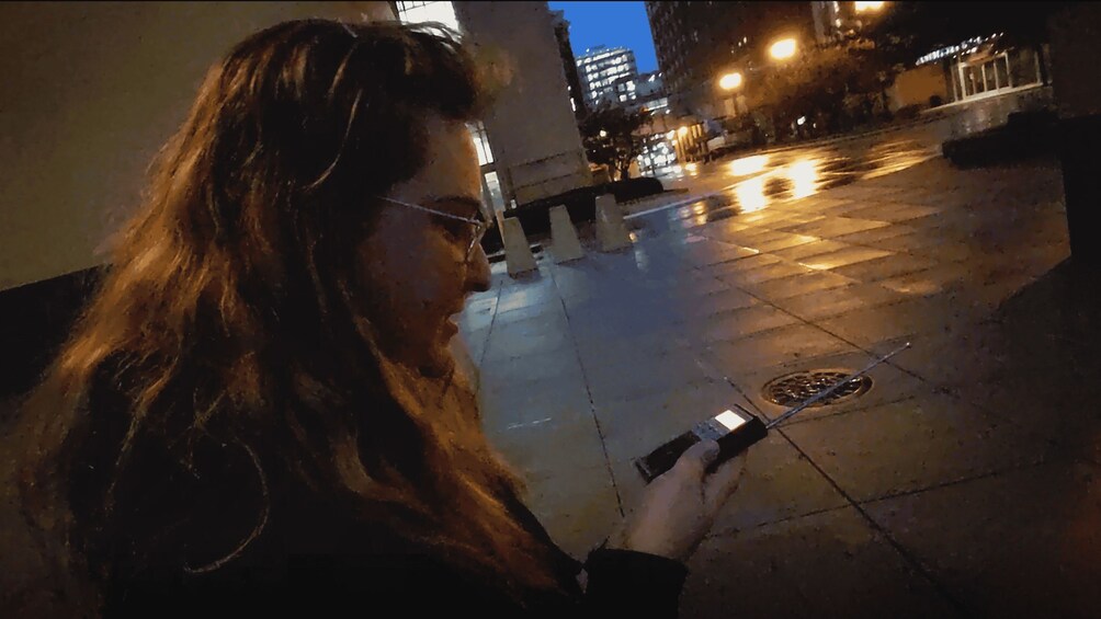 A person holding a smartphone on a city street at night. 3