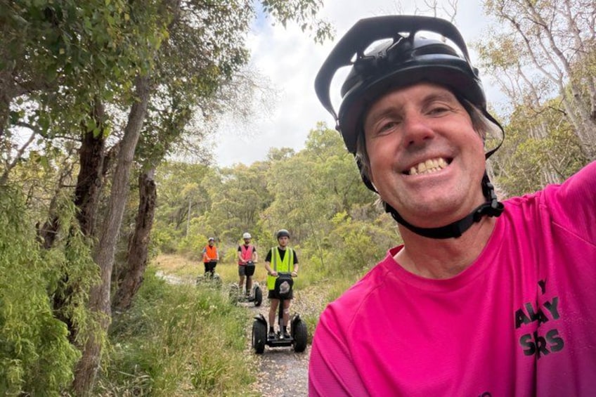 A person in a pink shirt and helmet, with three others on segways in a forested area. 4