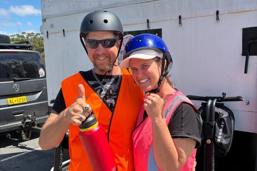 Two people wearing safety vests and helmets, standing in front of a vehicle. 5