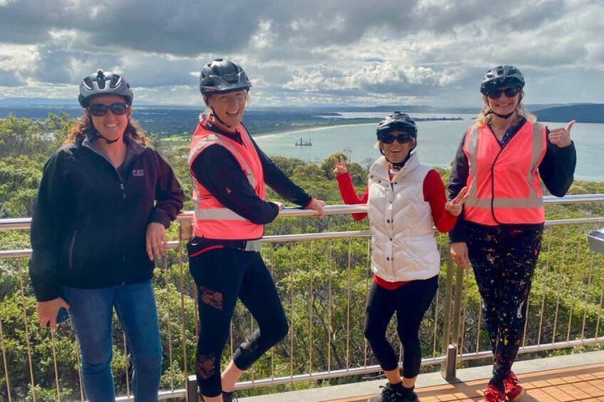 Four people wearing helmets and safety vests standing on a wooden deck overlooking a body of water and greenery. 3