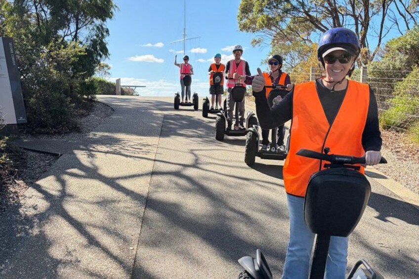 A person on a Segway giving a thumbs up, with others on Segways in the background. 1