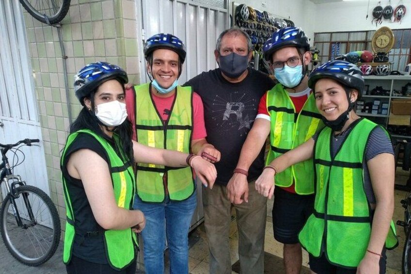 Four people wearing helmets and safety vests, standing in a room with bicycles and helmets on the wall. 3