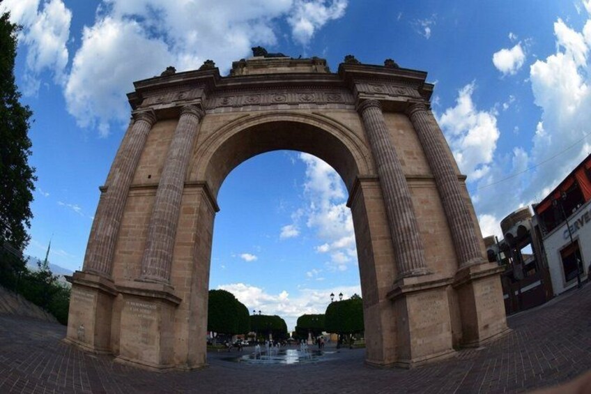 A large stone archway with columns, set against a clear sky with clouds. 5
