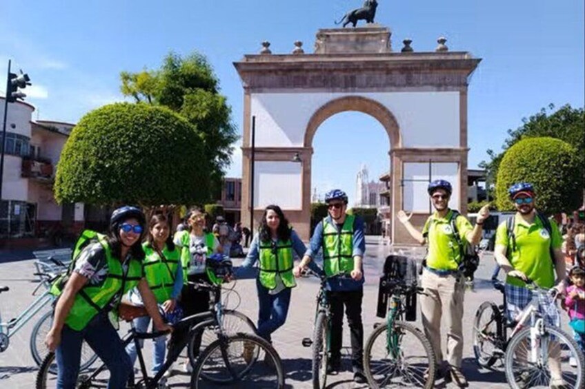A group of cyclists in front of a historical archway. 1
