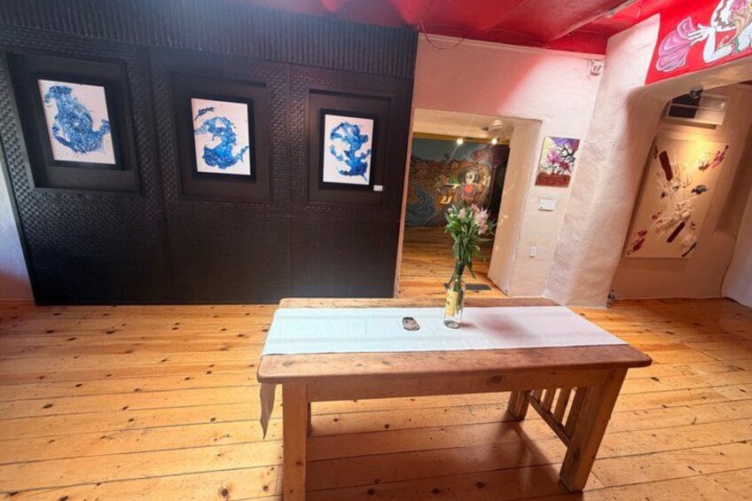 A wooden table with a vase of flowers, framed artwork on the wall, and a red sign in the background. 5