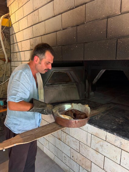 Una persona sostiene una sartén de metal con comida, de pie frente a un horno de ladrillo. 1