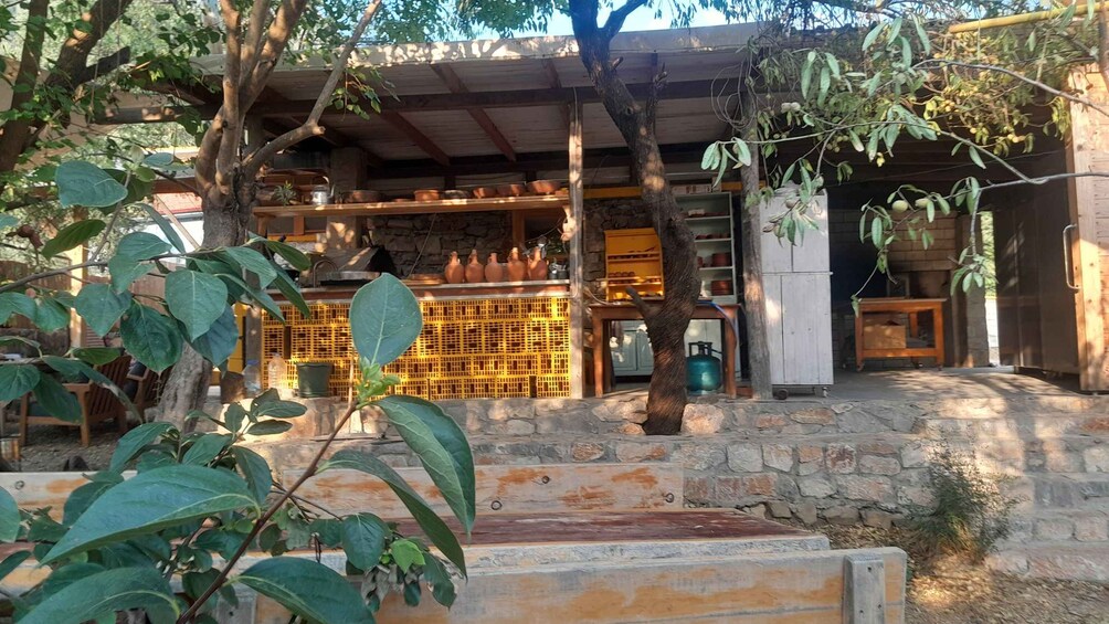 Un entorno rústico al aire libre con un muro de piedra, construcciones de madera y vegetación. 5