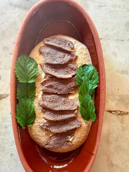 Un plato de terracota con carne en rodajas y hojas de menta. 4