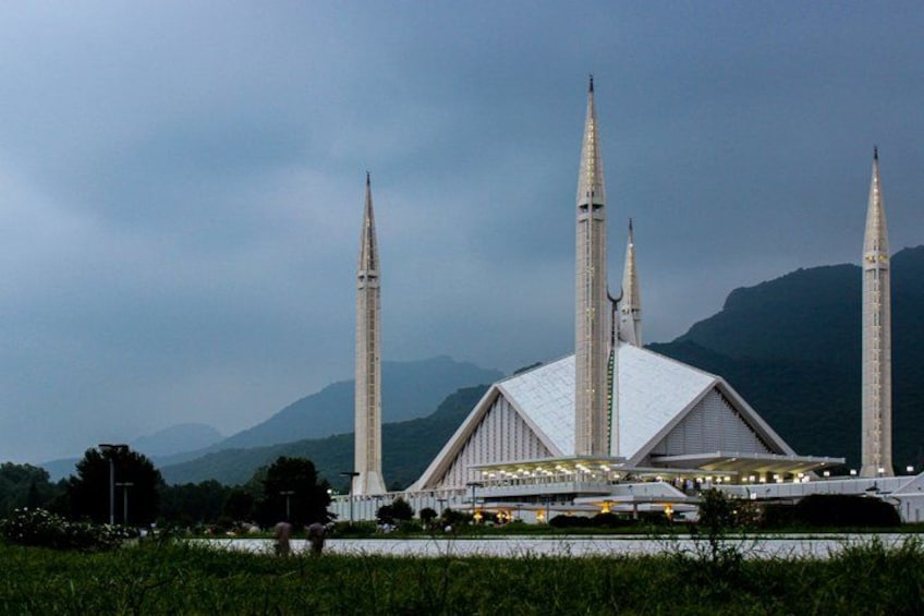 A large mosque with four minarets, surrounded by mountains and a cloudy sky. 1