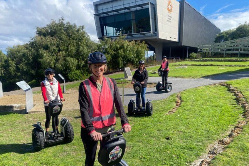 People riding Segways on a grassy path with a modern building in the background. 1