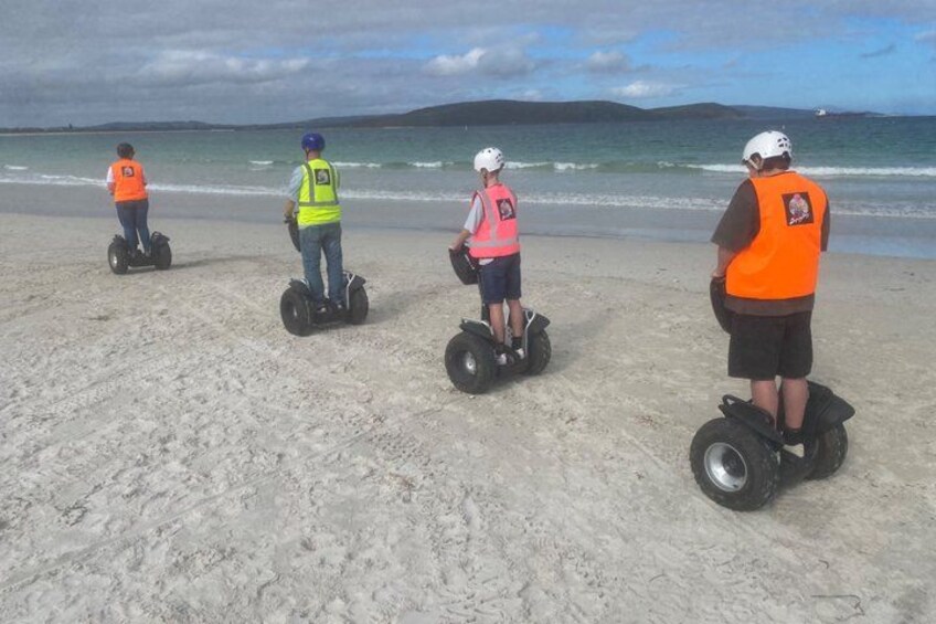 Four people on segways on a sandy beach with the ocean and hills in the background. 5