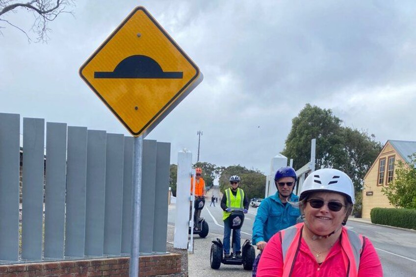 A road sign indicating a bridge ahead, a fence, and people riding Segways. 2