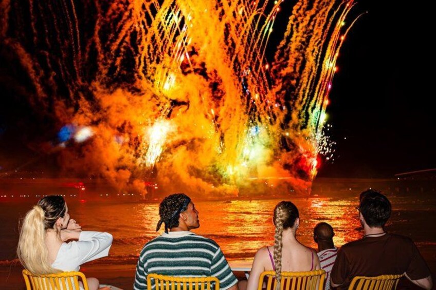 A group of people watching a fireworks display over water. 3