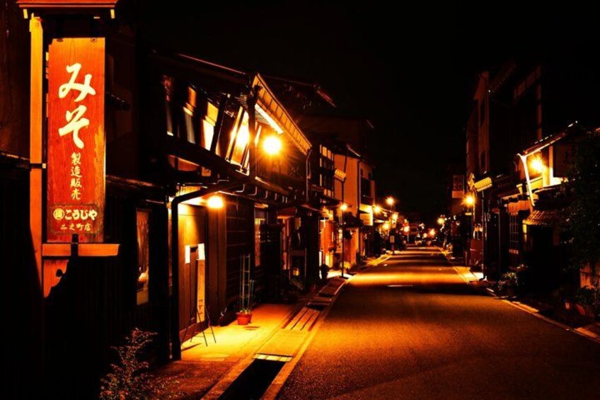 A narrow street at night with illuminated buildings and a sign with Japanese characters. 4