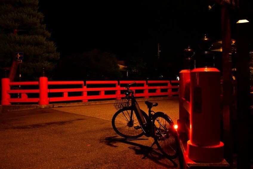 A bicycle parked near a red fence at night. 1
