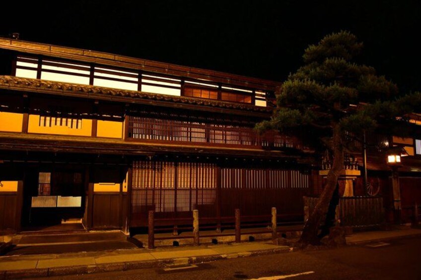 A traditional Japanese building at night with illuminated windows and a large tree in front. 2