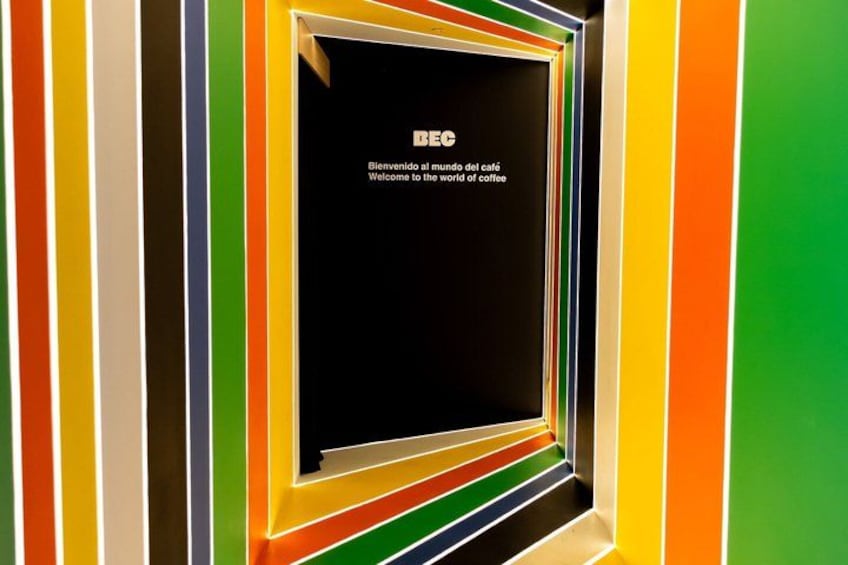 A colorful striped wall with a black sign that reads 'IEC Welcome to the world of coffee.' 2