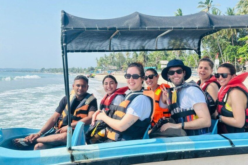 A group of people on a boat with life jackets, a canopy, and a beach with palm trees in the background. 1