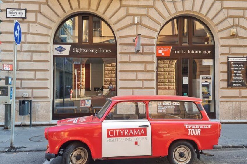 A red CITYRAMA Sightseeing Tours car parked in front of a building with large windows and a sign for Tourist Information. 2