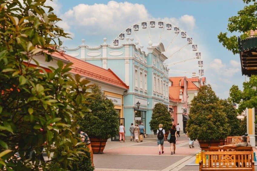 A Ferris wheel, a blue building, and people walking. 2