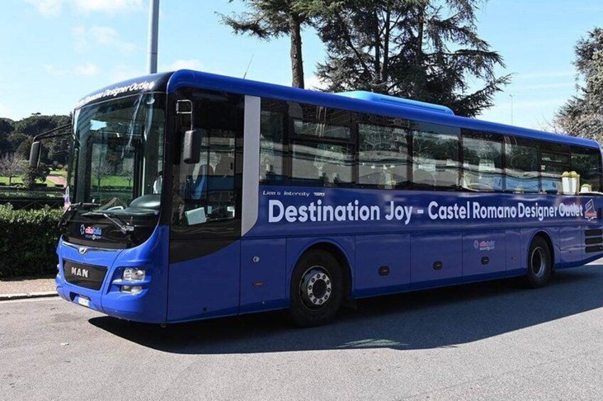A blue bus with 'Destination Joy - Castel Romano Designer Outlet' written on the side. 1