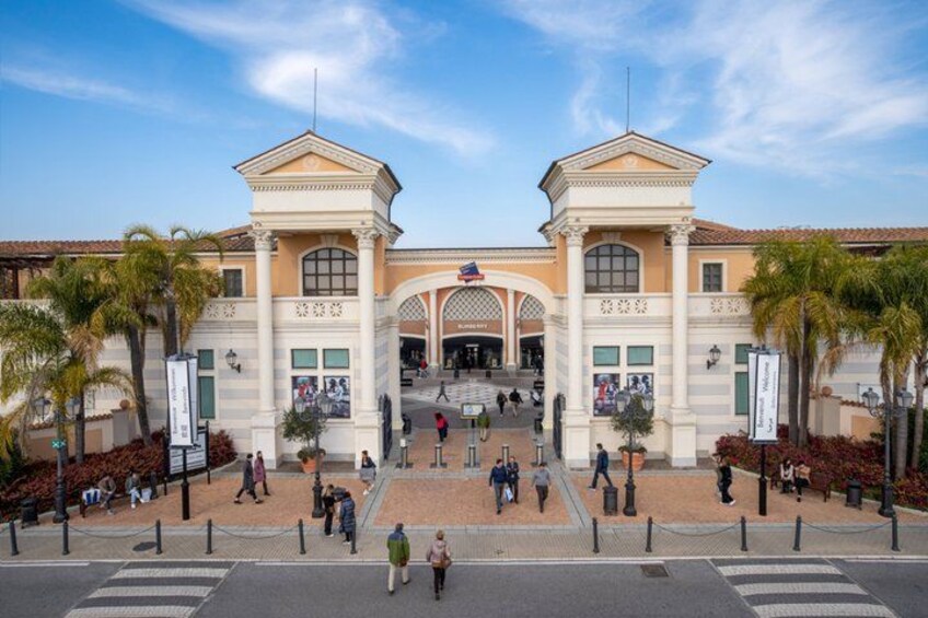 A large, historic building with a central archway, palm trees, and people walking in front. 3
