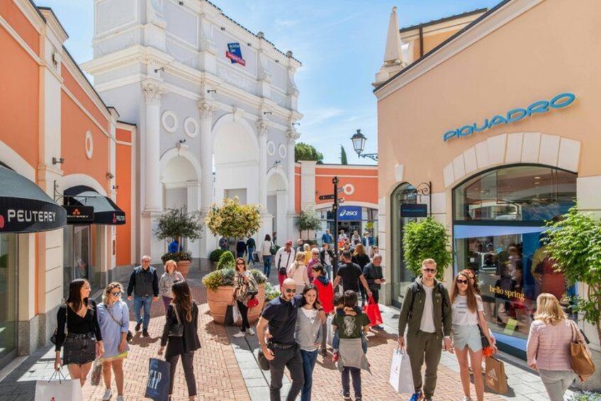 A busy pedestrian area with people walking, storefronts, and a prominent white building with arches. 4