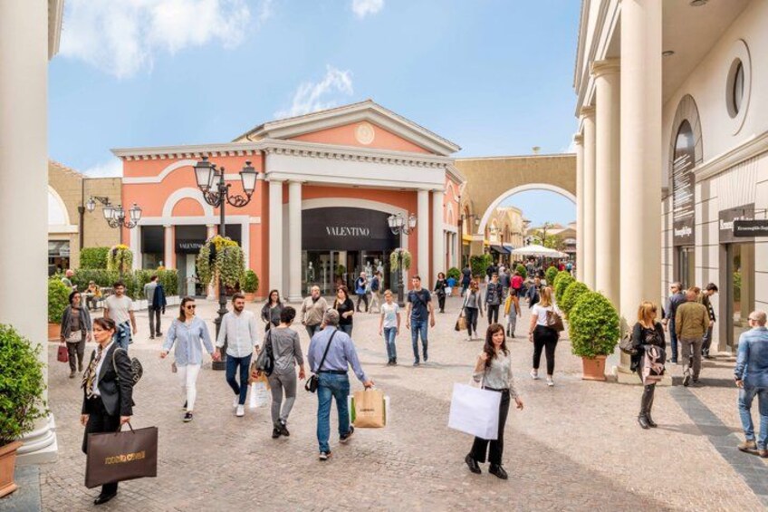 A pedestrian mall with people walking, a Valentino store, and a building with columns. 5