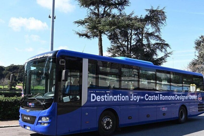 A blue bus with 'Destination Joy - Castel Romano Designer Outlet' on its side. 2
