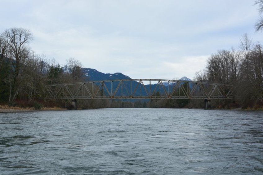 A metal bridge over a river with mountains in the background. 2