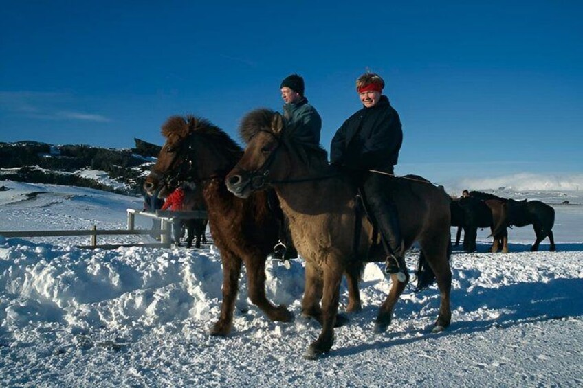 Two people riding horses on a snowy field with a clear sky. 4