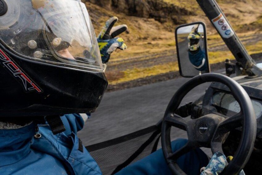 A driver in a racing suit and helmet inside a vehicle, with a steering wheel and a side mirror. 1