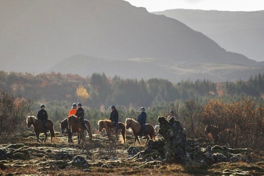 A group of people riding horses across a grassy field with mountains in the background. 5