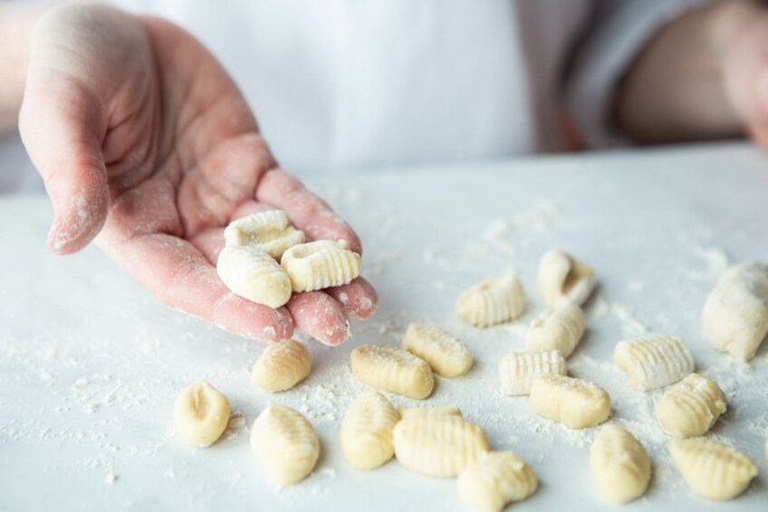 A hand holding small pasta shapes, with more scattered on a surface dusted with flour. 4