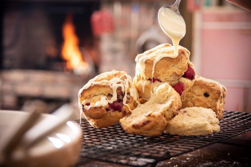 Biscuits with jam and a spoonful of cream being poured over them. 1