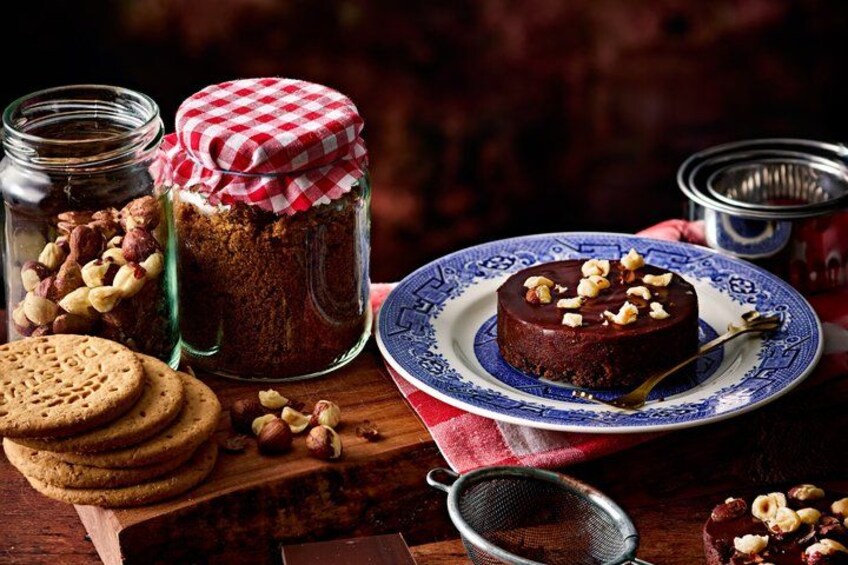 A chocolate cake on a plate with nuts, cookies, and jars of ingredients on a wooden table. 4