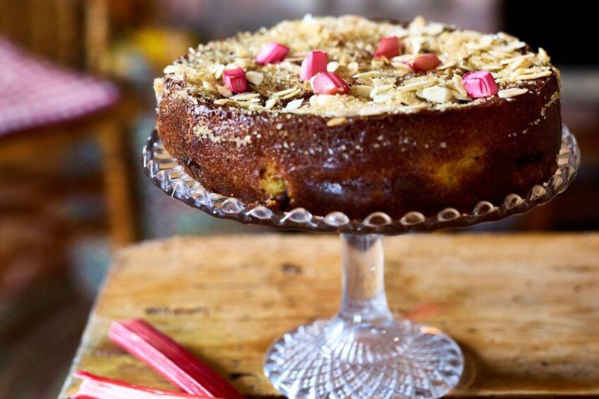 A round cake on a glass cake stand with a wooden table and chairs in the background. 5