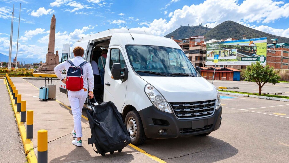 A white van parked in a parking lot with a person exiting and carrying luggage. 2