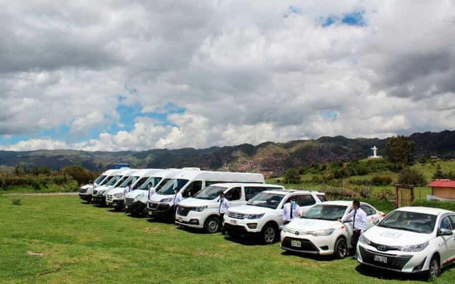 A row of white vehicles parked on a grassy field with mountains in the background. 5