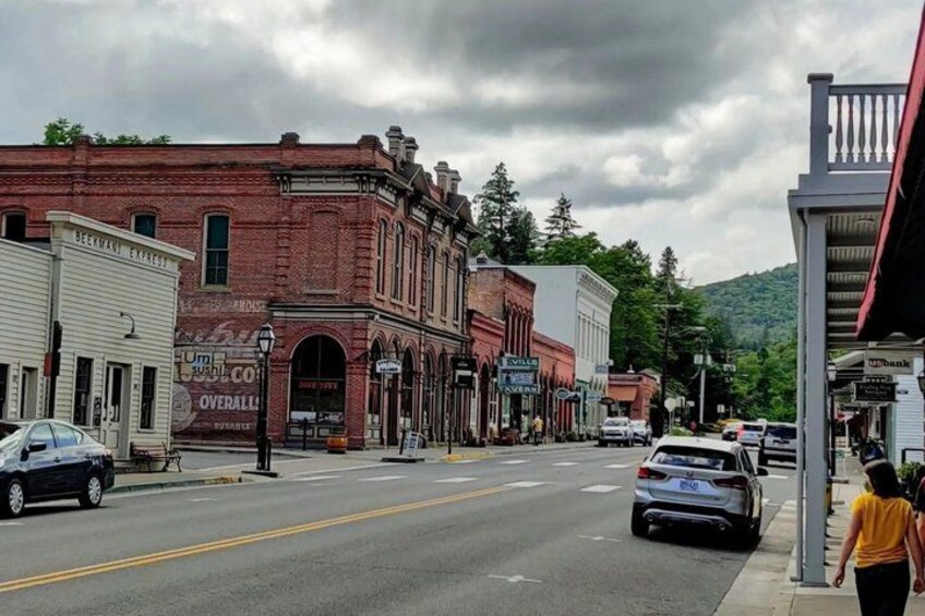 A street lined with historic buildings, a parked car, and a person walking on the sidewalk. 3