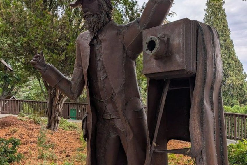 A statue of a man with a beard and a suit, standing next to a rusted metal structure. 4